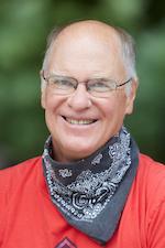 portrait image of Dr. Tom Stoffregen, smiling in a red shirt, blue kneck handkerchief, wire rim glasses
